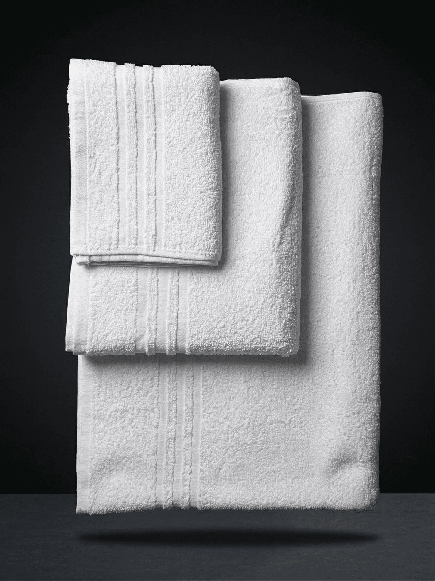Set di 3 asciugamani bianchi in puro cotone per hotel, linea Classic, piegati e impilati su sfondo scuro