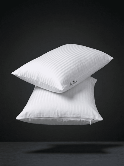 Una fotografia professionale di alta qualità e pulita di due federe di cotone bianco, impilate in modo minimalista e che fluttuano in un ambiente di studio scuro con illuminazione drammatica. Le federe sono di un bianco pulito, ben stirate e la loro forma è ben definita, mostrando la consistenza del tessuto in cotone di qualità. Una leggera ombra morbida è proiettata sulla superficie grigia sottostante, creando un effetto di profondità e leggerezza. Lo sfondo è un nero profondo e sfumato. Questa immagine es